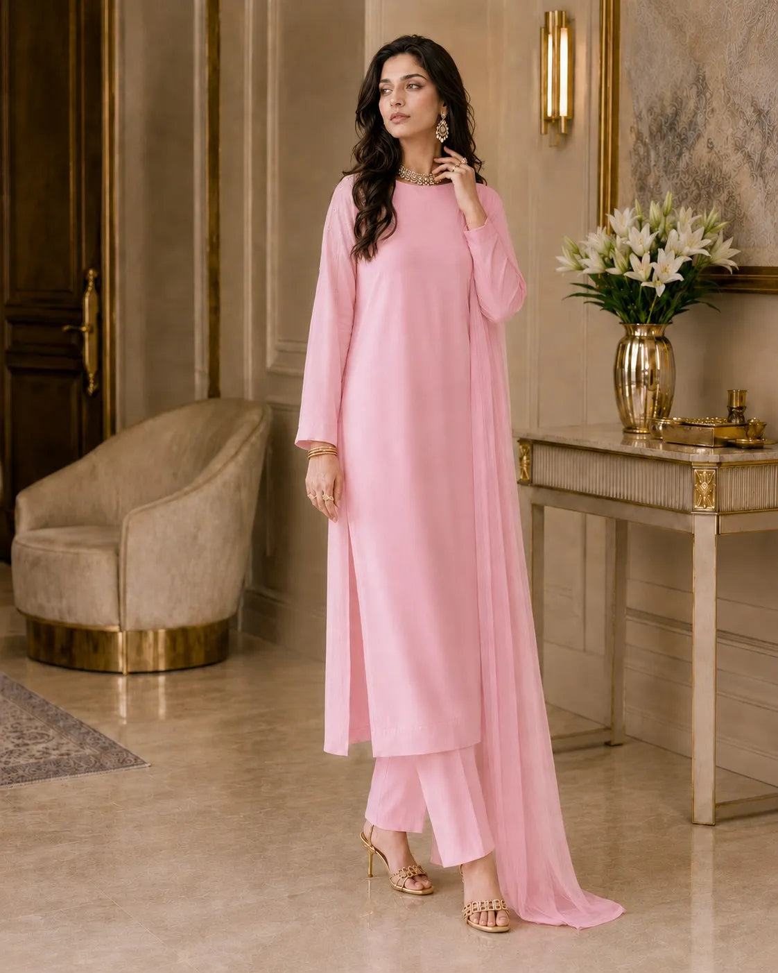 Woman in a pink outfit standing in an elegant room with a table and chair.