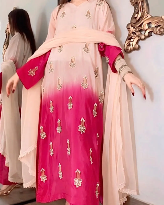 Woman wearing a pink and red traditional outfit with gold embroidery, standing in front of a decorative mirror.