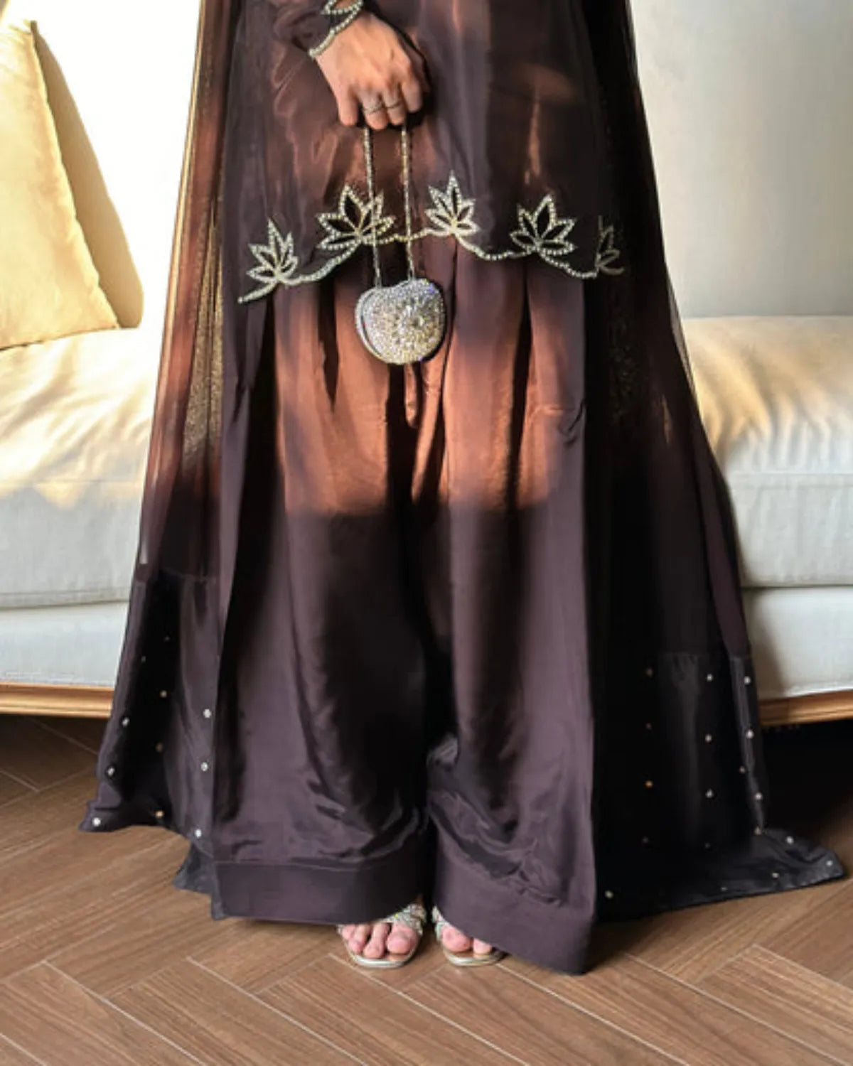 Person wearing a dark brown outfit with a decorative bag, standing on a wooden floor.