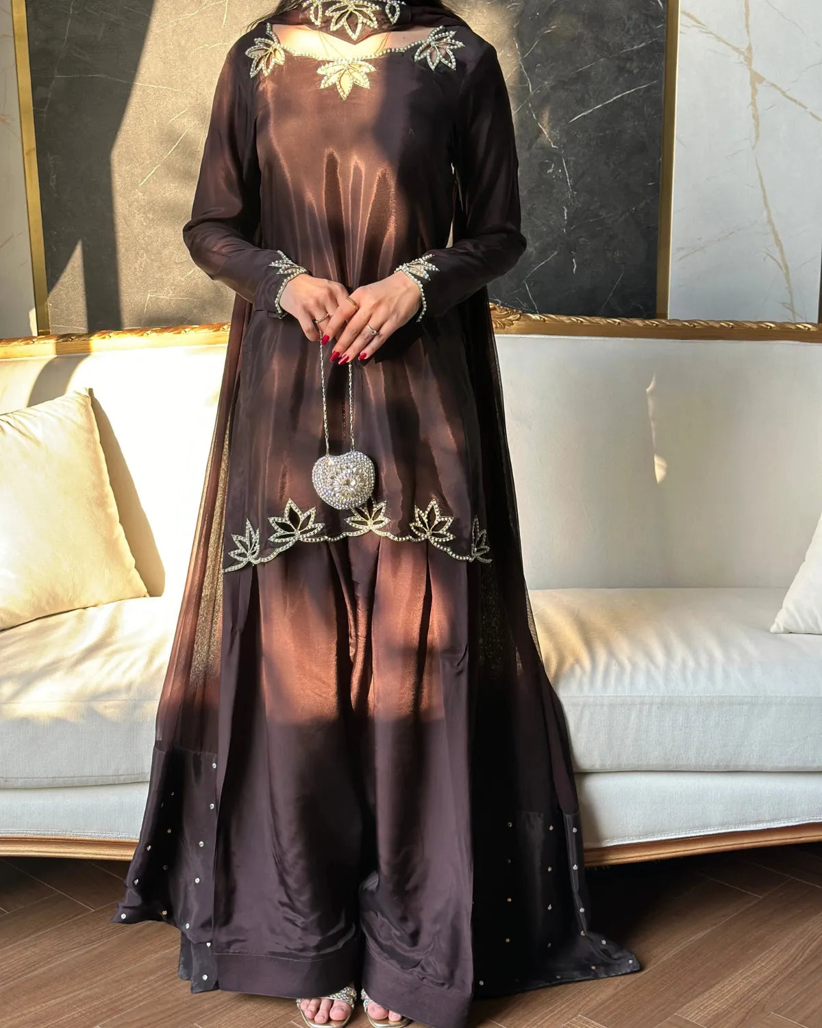 Long dark dress with floral embroidery in a room with a couch and wall art.
