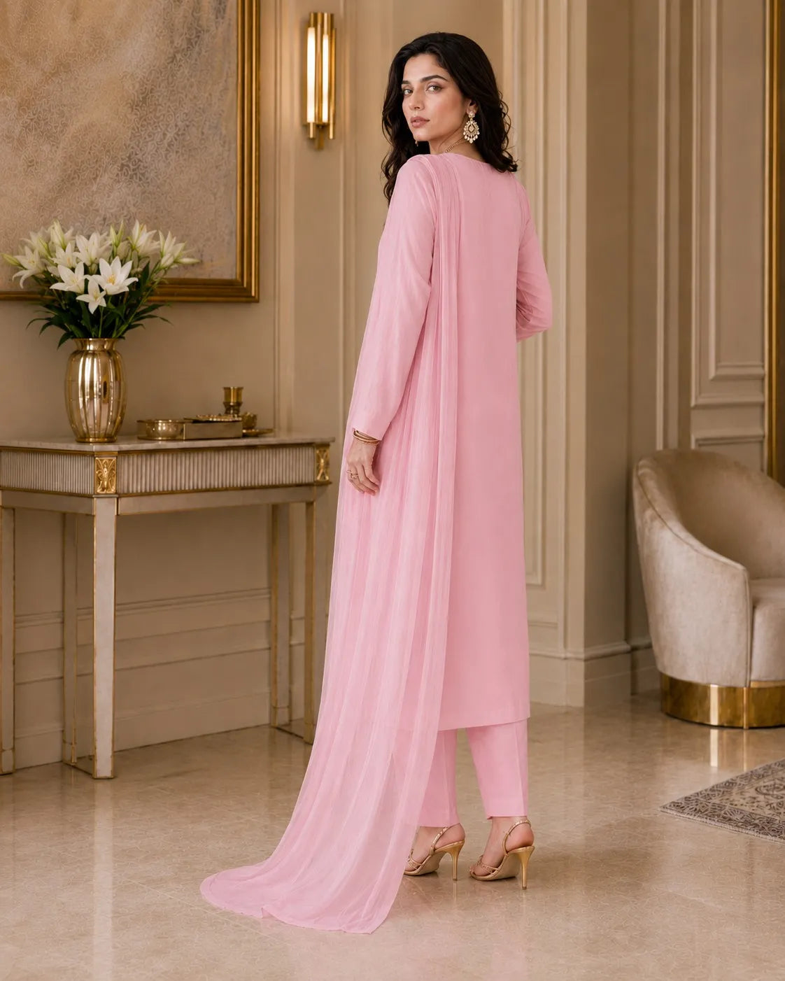 Woman in a pink outfit standing in an elegant room with decor elements.