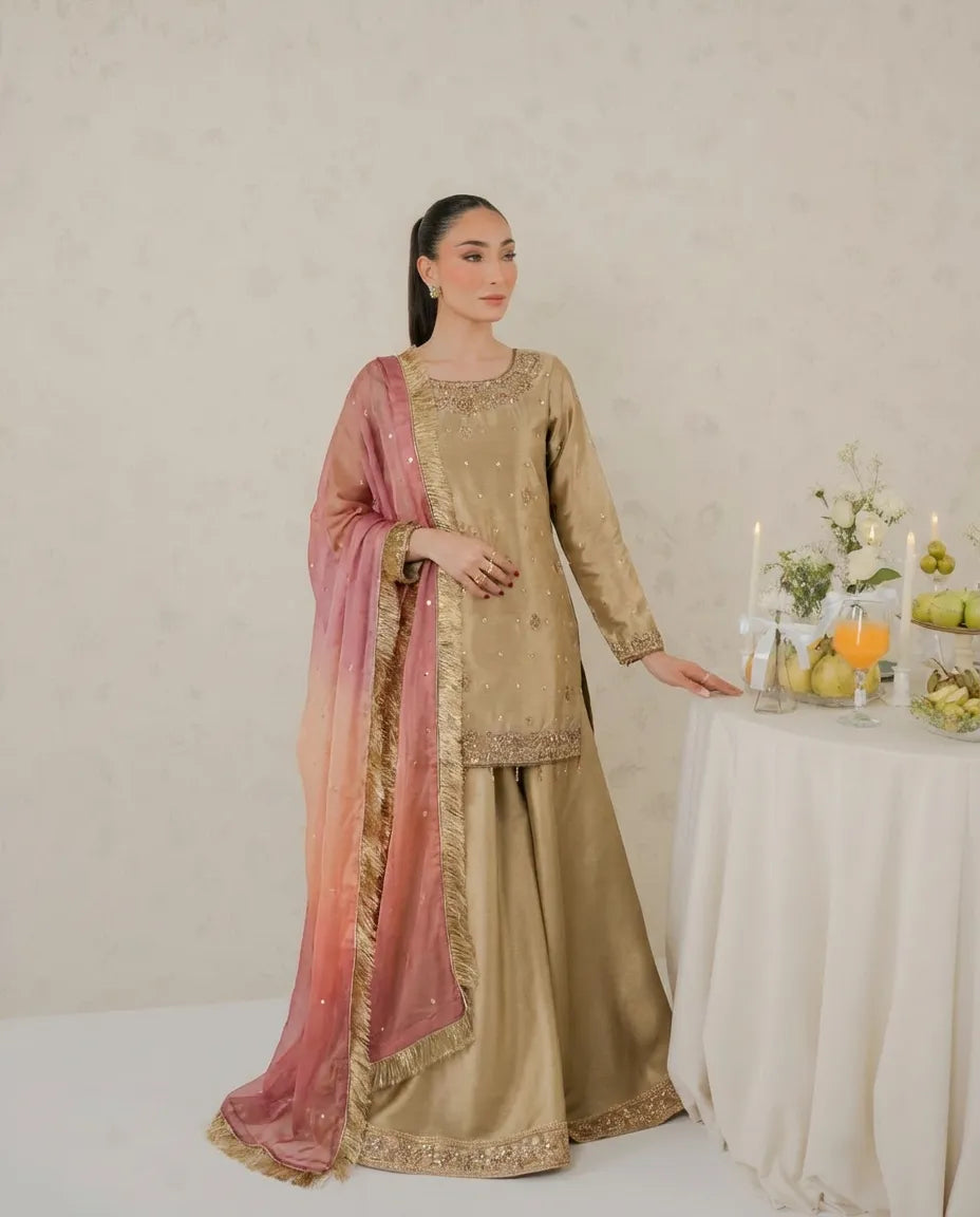 Woman in traditional beige and pink outfit standing next to a table with fruits and candles.