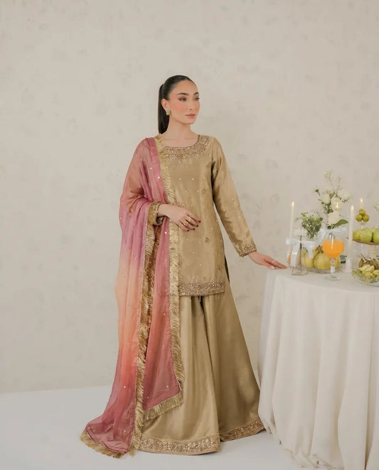 Woman in traditional beige and pink outfit standing next to a table with fruits and candles.