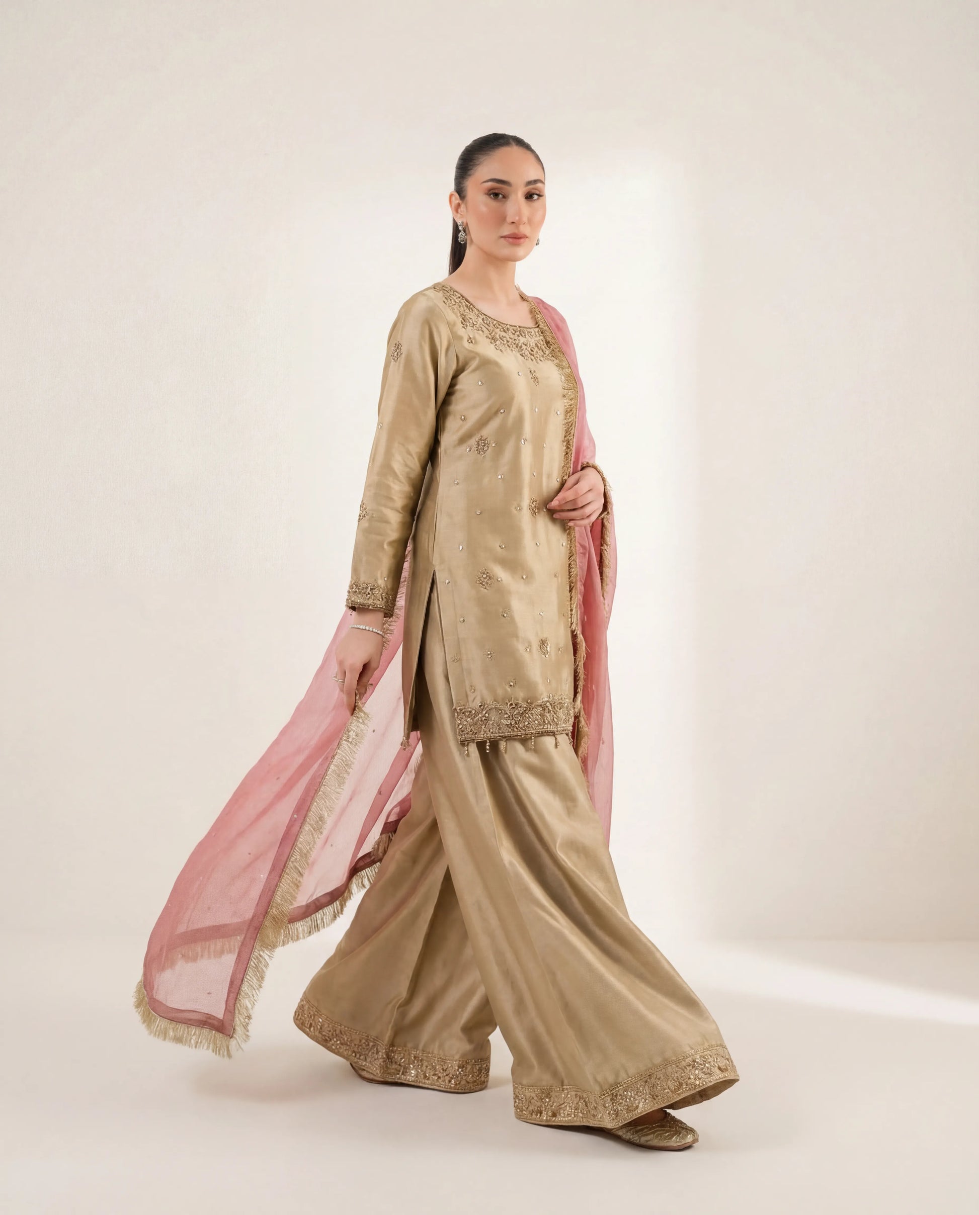 Woman wearing a traditional beige outfit with pink dupatta on a white background