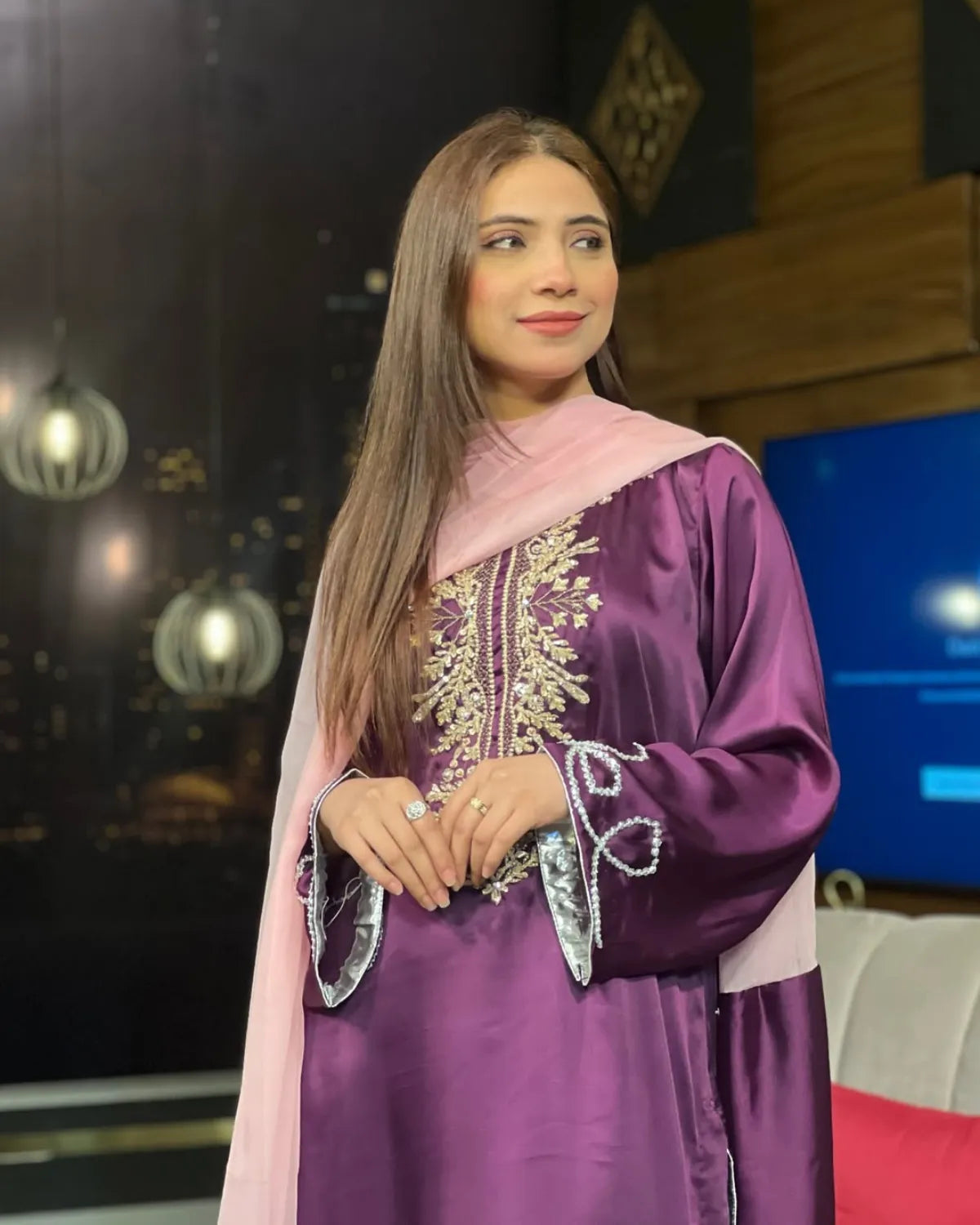 Woman wearing a purple traditional outfit with gold embroidery in a studio setting.