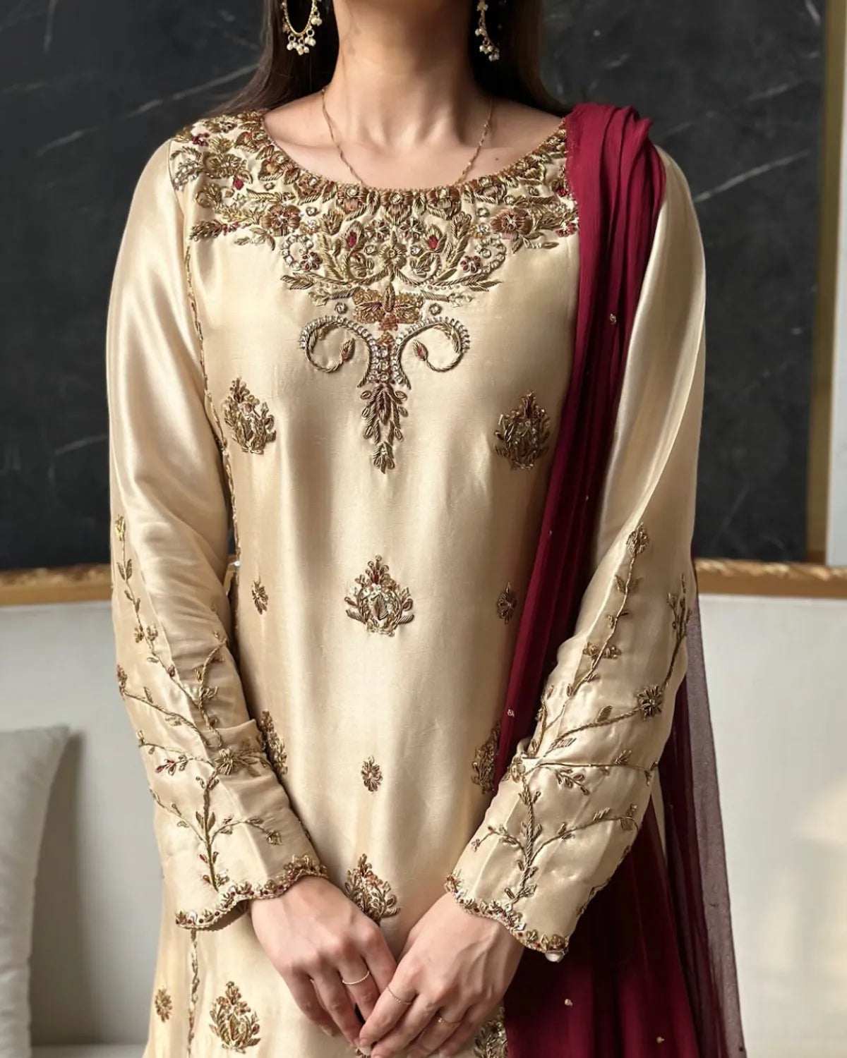 Beige embroidered traditional outfit with maroon dupatta against a dark background