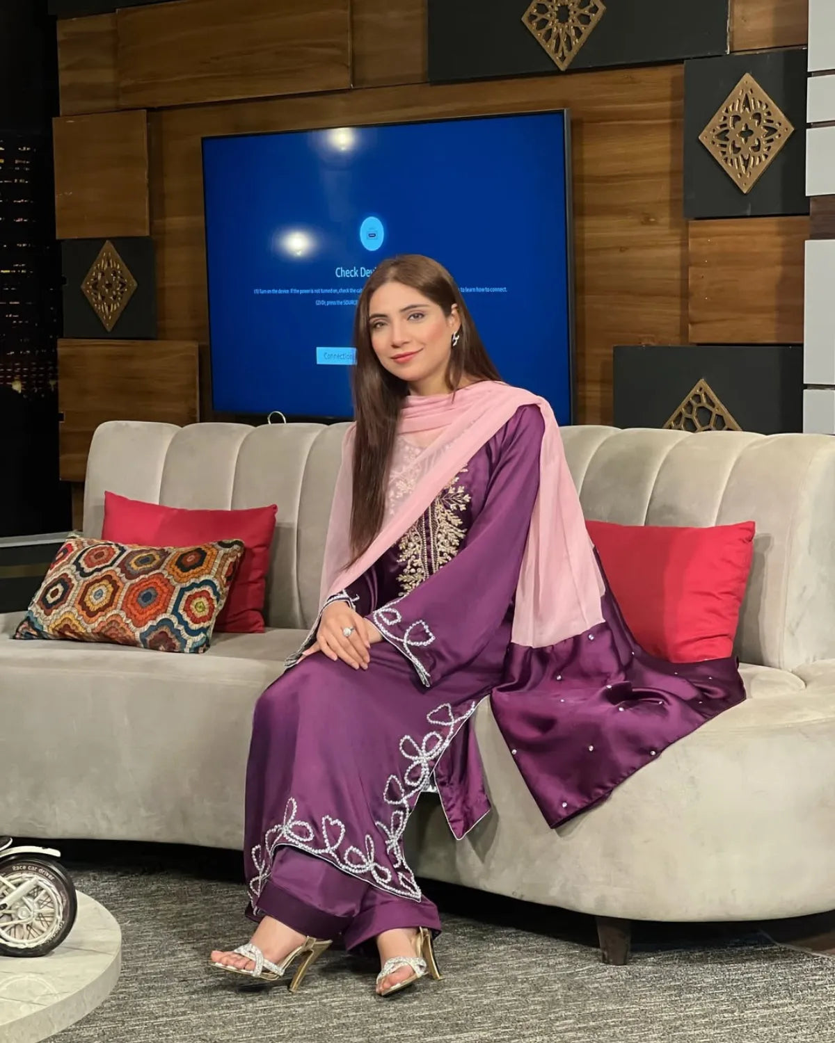 Woman in a purple traditional outfit sitting on a couch with a television in the background