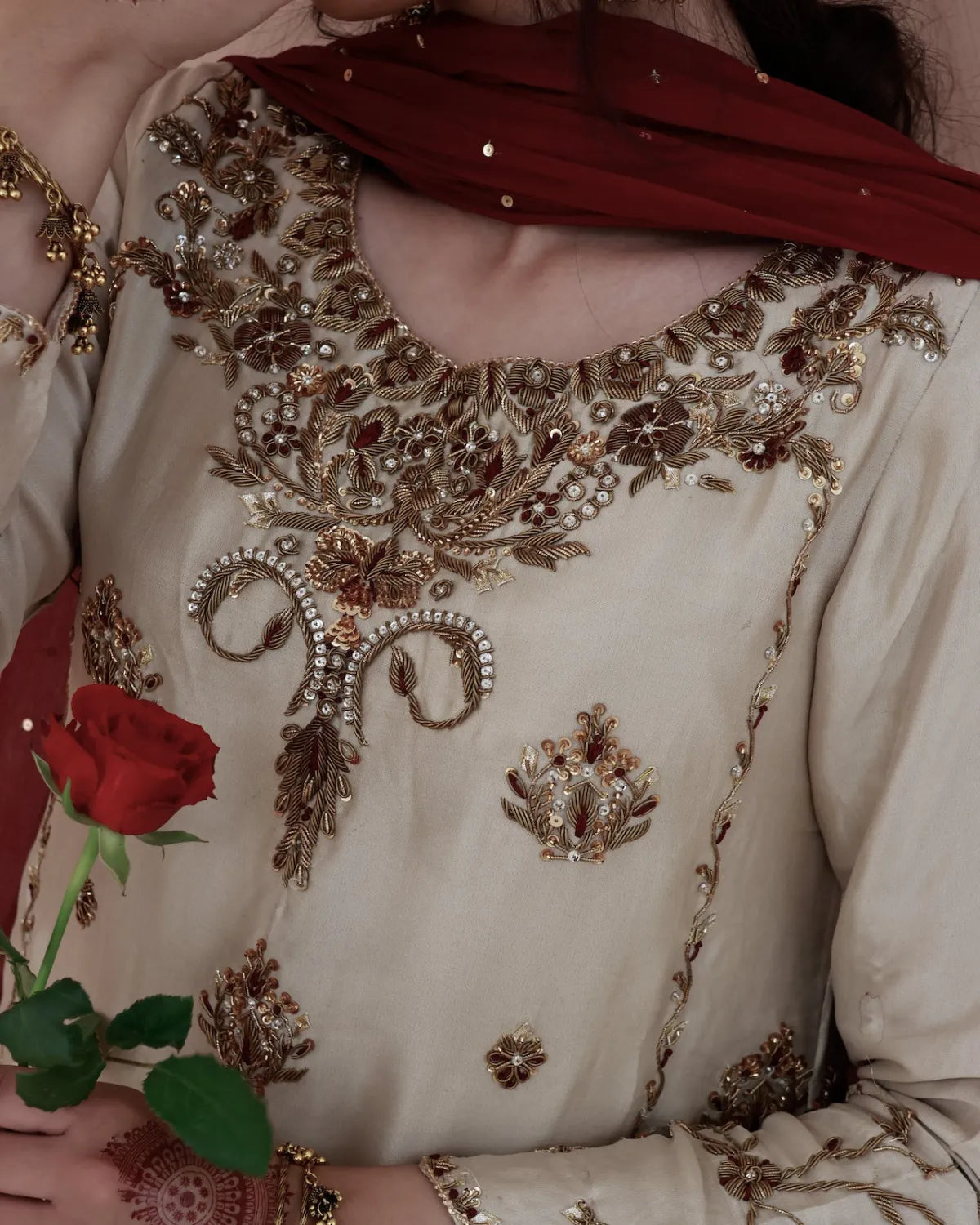 Close-up of a person wearing a heavily embroidered traditional outfit with a red rose held in hand.