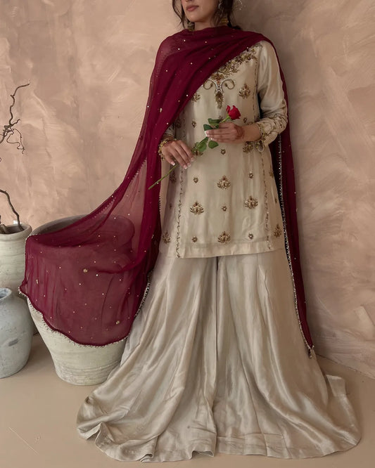 Woman wearing an embroidered traditional outfit with a maroon dupatta against a neutral background