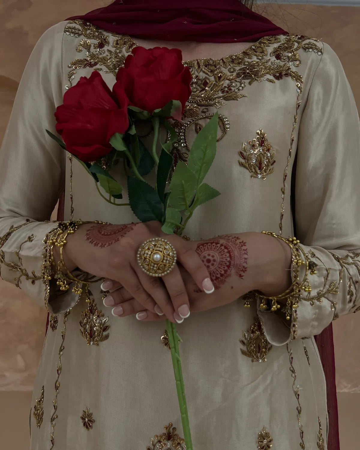Person wearing an embroidered outfit holding red roses with a blurred background