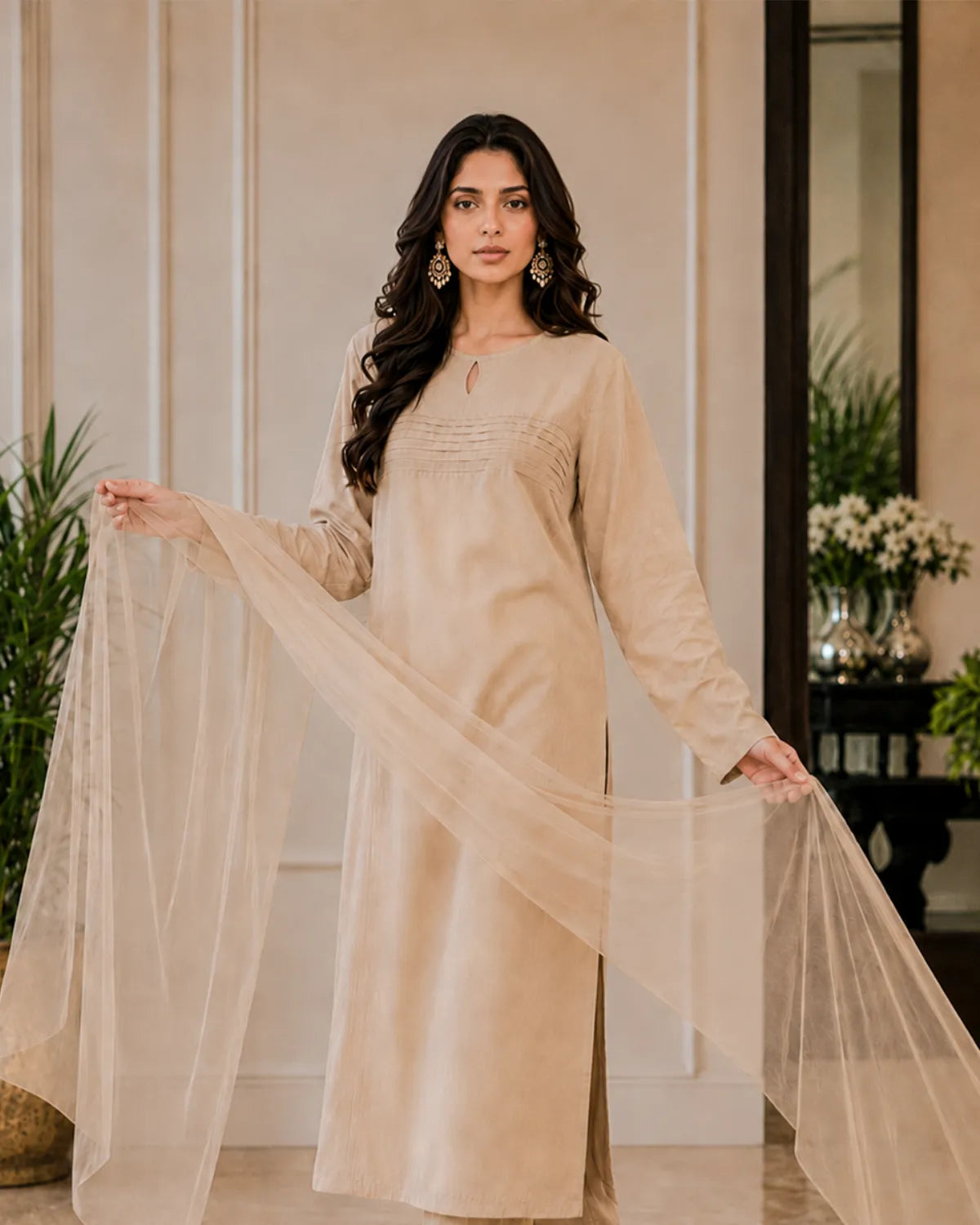 Woman in a beige traditional outfit holding a dupatta in an indoor setting.