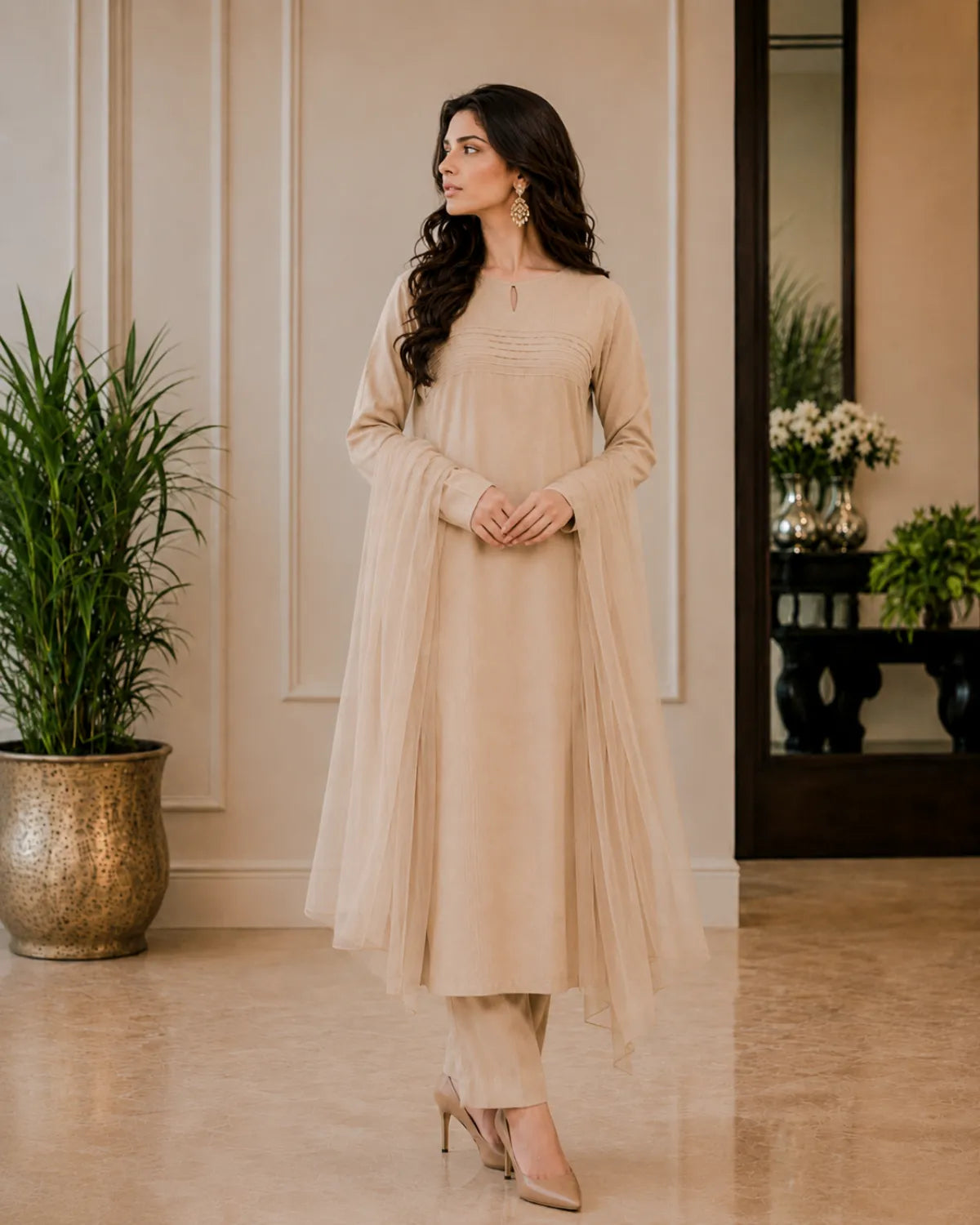 Woman in a beige traditional outfit standing in a room with plants and decor.