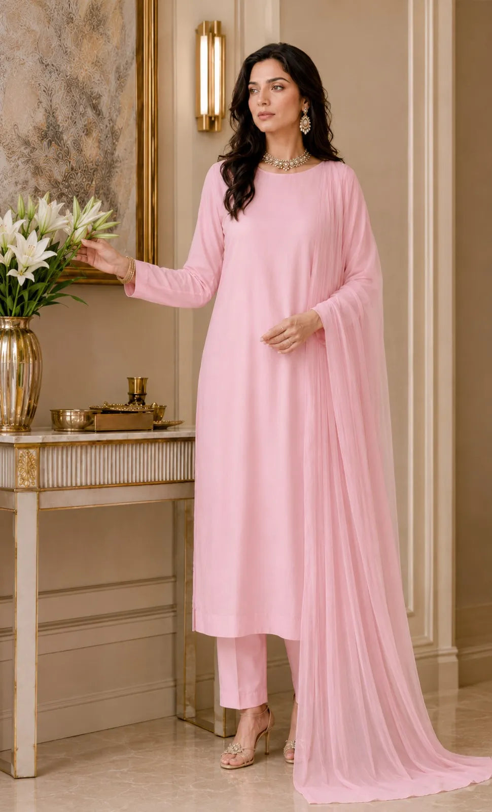 Woman in a pink traditional outfit standing in an elegant room with floral decorations.