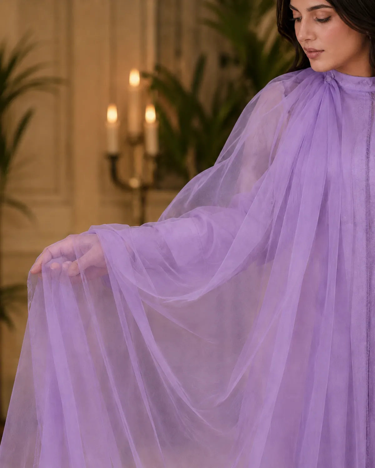 Woman wearing a flowing purple dress in an elegant indoor setting with candles and plants.