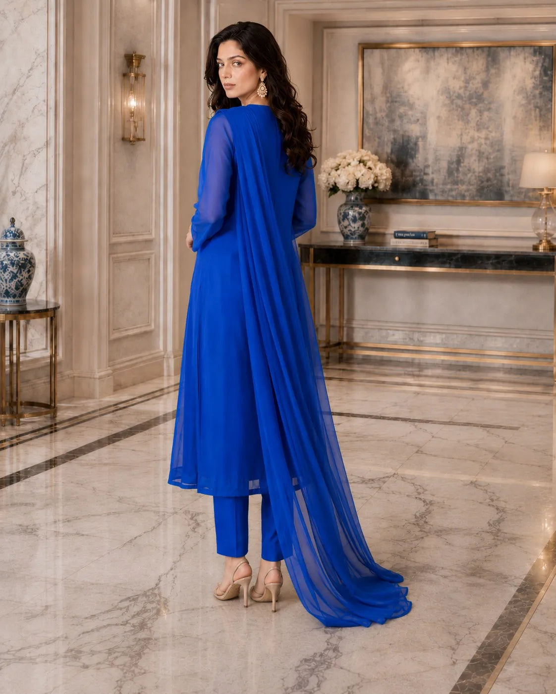 Woman in a blue outfit standing in an elegant interior setting.