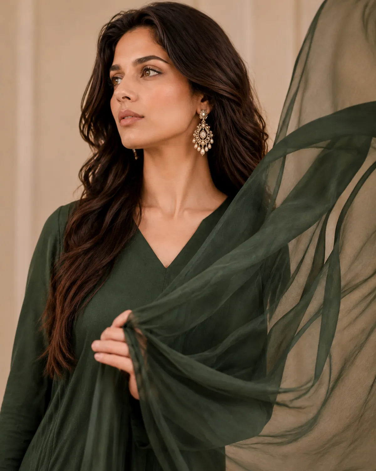 Woman wearing a dark green dress with a sheer green fabric draped over her shoulder against a beige background